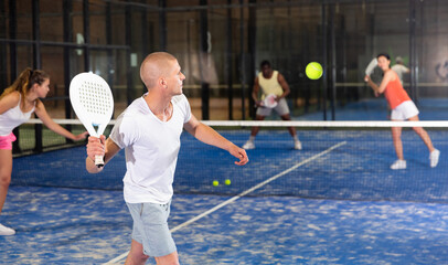 Professional male player ready to hits the ball while playing padel at fitness health club