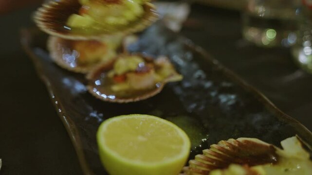 Woman hand placing garnish on scallops in upscale restaurant setting with elegant black plate and fresh lemon, capturing the essence of fine dining and culinary artistry.