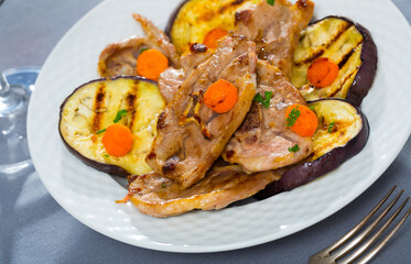 Delicious broiled lamb loin chops served on white plate with grilled eggplant and carrots..