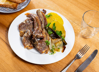 Appetizing fried lamb ribs served on platter with potatoes and peppers