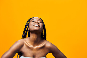 A joyful young African woman with braided hair smiles against a bright yellow background, radiating...