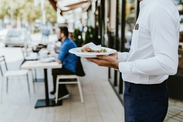 Fototapeta premium Waiter presents a beautifully plated thai dish to diners at a charming sidewalk restaurant in a lively outdoor setting