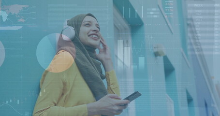 Image of financial data processing over biracial woman in hijab using smartphone on the go