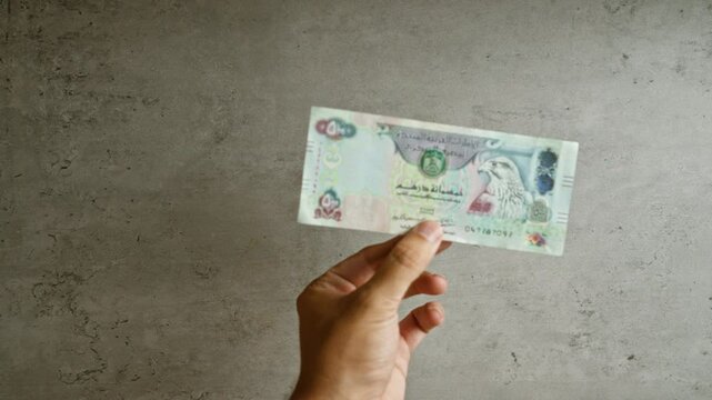 Hand holding uae dirham note against concrete background showing currency from united arab emirates