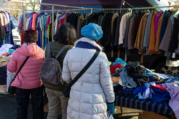 Women rummaging through piles of cheap clearance clothing at an outdoor flea market in Galicia,...