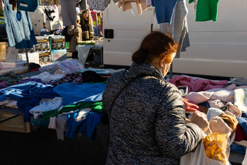 Older lady looking at lots of clothes at an outdoor flea market with cheap and clearance items in...