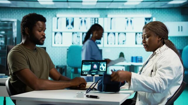 Black medic measuring the blood pressure and pulse of a male patient, doing routine checkup with a blood pressure monitor. Physician using advanced tools for cardiology readings. Camera B.