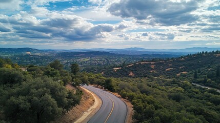 Winding road through scenic hills, aerial view, cloudy sky, valley background; travel, tourism