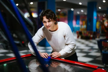 Fototapeten Young man enjoys playing air hockey in a vibrant arcade setting © callisto