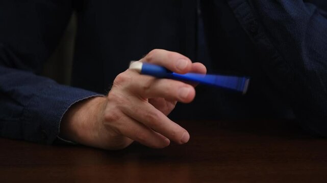 man is sitting at table and nervously twirling ballpoint pen in his hands. a businessman is nervous during negotiations, meetings. close-up of fingers holding a ballpoint.