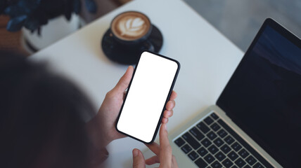 Cell phone white screen mockup, Woman hand holding mobile phone with blank screen while working at coffee shop. Business woman using smartphone, mockup for social media marketing