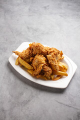 Fried chicken on a bed of French fries on a marble background