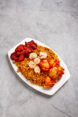 chinese food of sweet and sour chicken with fried rice, shrimp, pork ribs, on white plate with marble background