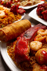 Chinese pork ribs with broaster chicken, fried rice, spring roll, shrimp on white plates, served in a table