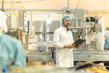 Inspector checking automated machinery in food production facility Focus on quality control safety and workflow efficiency. Worker overseeing food packaging machinery in a modern manufacturing plant.