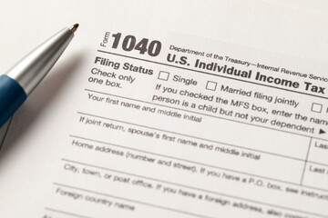Close-up view of a 1040 U.S. Individual Income Tax Return form with a pen placed on it,...