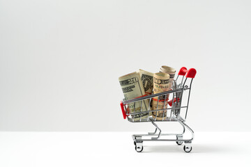 Red miniature shopping cart filled with US dollar banknotes isolated on white background, concept of inflation or budgeting © Kenishirotie