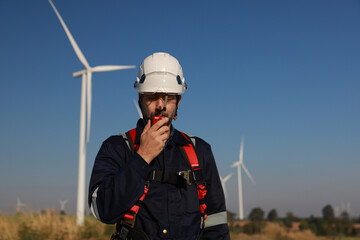 A male maintenance technician in uniform uses a talkie to work on a station wind turbine. Carbon neutrality and clean energy.