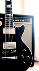 Close-up of a black electric guitar with a blurred amplifier in the background.