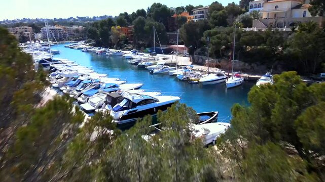 Explore the tranquil beauty of Santa Ponsa's harbor, surrounded by lush greenery and colorful homes. Experience this picturesque location in Mallorca, capturing the essence of coastal charm.