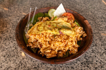 Fried rice with egg and vegetables served on a clay plate with a banana leaf base
