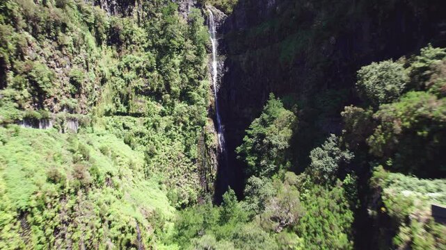 Cascading waterfall in a serene valley nestled between lush green mountains at the 25 fontes levada in Madeira, Portugal in 4k aerial drone