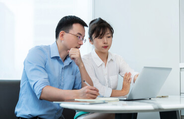 Obraz premium Two asian businesspeople working together in the office while using laptop