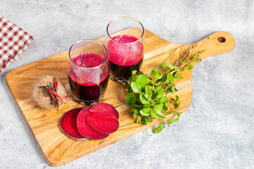 A wooden board with beetroot slices, a whole beet, fresh mint sprigs, and two glasses of fresh beet...