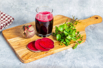 a glass of beetroot juice, fresh beet slices, a whole beetroot, and mint leaves on a wooden board.