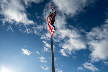 A flag waves against a bright blue sky dotted with fluffy white clouds.  The sun shines brightly, illuminating the scene.