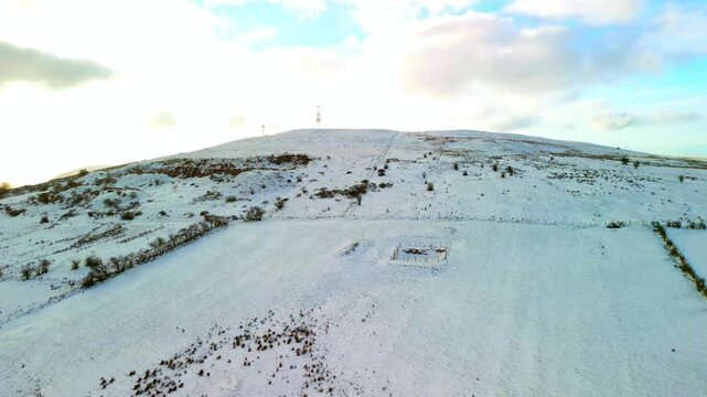 Aerial shot of Cavehill in Belfast, Northern Ireland on a snowy and calm winter day. The camera travels forwards, over a snow covered mountain. Shot in 4K, 60fps with Rec709 color.
