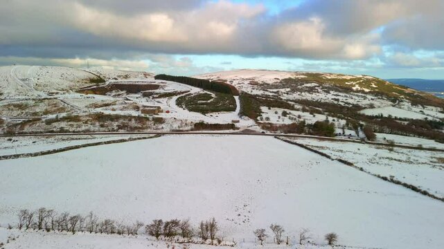 Aerial shot of Cavehill in Belfast, Northern Ireland on a snowy and calm winter day. The camera advances over a snow covered field revealing a snowy mountain. Shot in 4K, 60fps and in Rec709 color.