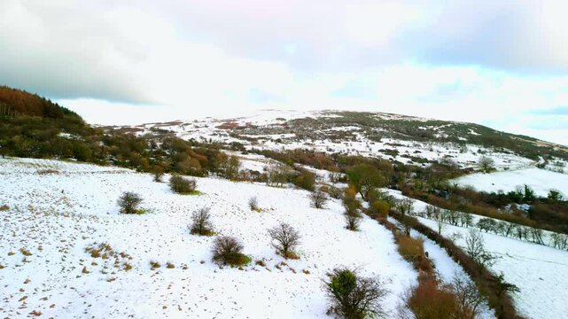 Aerial shot of Cavehill in Belfast, Northern Ireland on a snowy and calm winter day. The camera travels over a snow covered path and revealing a snowy mountain. Shot in 4K, 60fps with Rec709 color.