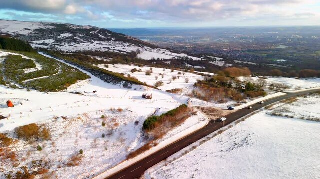 Aerial shot of Cavehill in Belfast, Northern Ireland on a snowy and calm winter day. The camera moves left to right, over the mountains and passing cars. Shot in 4K, 60fps and in Rec709 color.