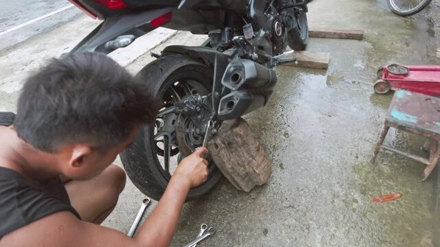 Street mechanics in the Philippines change motorcycle tires at a local vulcanizing shop. This hands-on repair work highlights Filipino craftsmanship and street culture in an urban setting