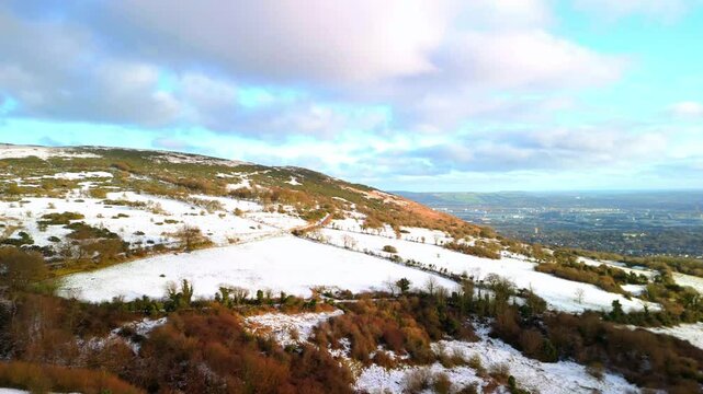 Aerial shot of Cavehill in Belfast, Northern Ireland on a snowy and calm winter day. The camera moves left to right over the mountain, revealing Belfast City. Shot in 4K, 60fps and in Rec709 color.