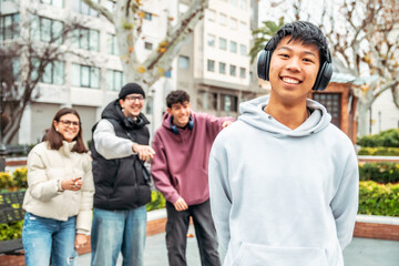Happy and smiling multiracial group of students having fun together in a university campus, a chinese teenager with headphones is smiling and his friends are pointing at him