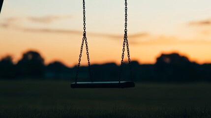 Sunset silhouette of empty swing set in field.