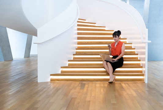 Woman sitting on staircase using smart phone and laptop