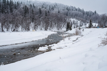A beautiful river gracefully winds its way through a picturesque snowy forest, with majestic trees completely blanketed in soft, white snow all around them, creating a winter wonderland