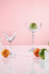 Cosmetics advertising photo with party concept, against a pink backdrop. An empty space for positioned products, next to cocktail glasses, decorated with some lemon fruits, placed on a glass surface.