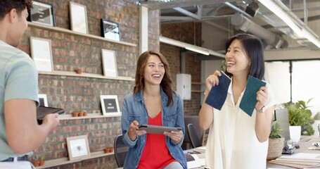 Showing fabric samples, multiracial women discussing interior design ideas in modern office