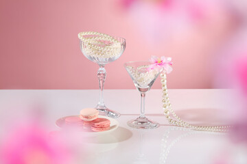 A plate of macarons, a few pearl-string glasses, pink flowers, and an empty space for product displays are shown in front. The background is pink. A party-themed advertisement for cosmetics.