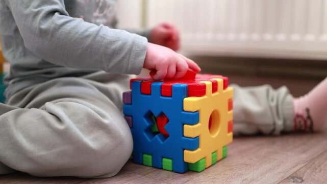 Little girl playing on the floor of the children's room with a colorful Montessori cube, educational toys for children, children's logic games, happy child with her toys