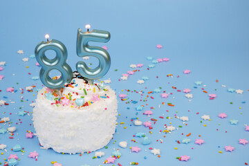 Coconut birthday cake with burning candles, anniversary 85 years and many colorful sprinkles on...