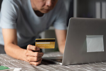 Senior man making an online purchase with a credit card while leaning towards his laptop