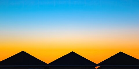 Silhouetted rooftops with triangular shapes against a gradient blue and orange sunset sky with ample copy space at the bottom for text.