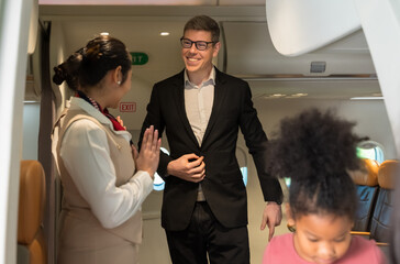 Businessman passenger in dark suit smiling and conversing with air hostess or cabin crew while leaving airplane cabin. Flight attendant standing at airplane entrance door and greeting passengers . Air
