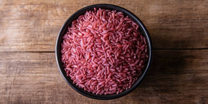 Raw red-skinned Jasmine rice in a black bowl on a rustic wooden background highlighting Asian culinary specialties with vibrant colors and textures.