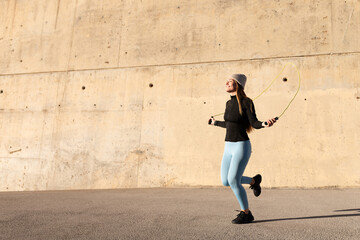 Sportswoman jumping rope in front of concrete wall during winter training